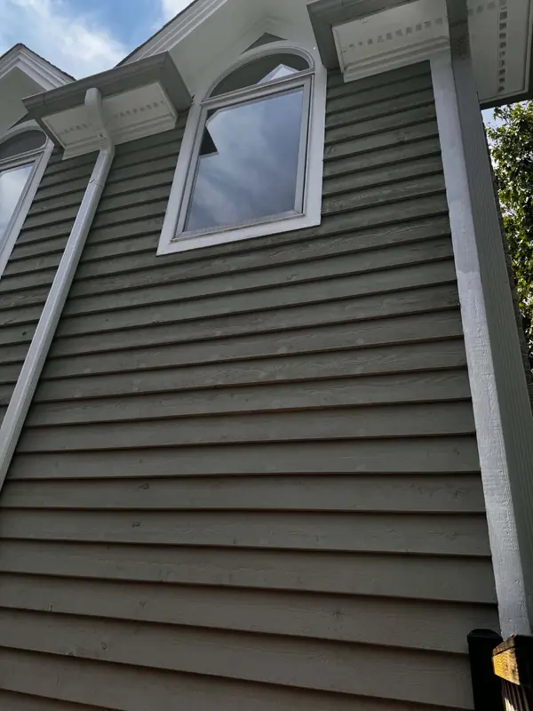 Two-story exterior with green lap siding and freshly painted white trim and brackets