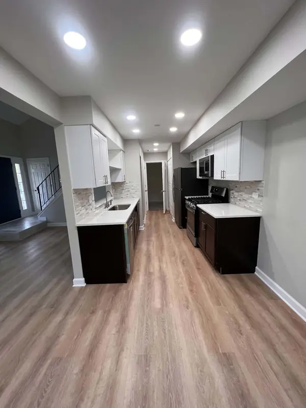 Galley kitchen with white upper and espresso lower cabinets, recessed lights and wood-look flooring