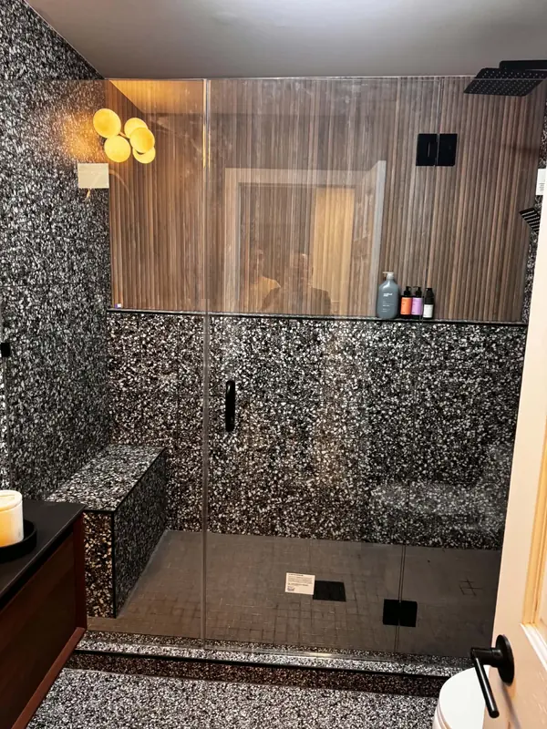 Terrazzo tiled shower with a built-in bench, fluted wood wall and frameless glass